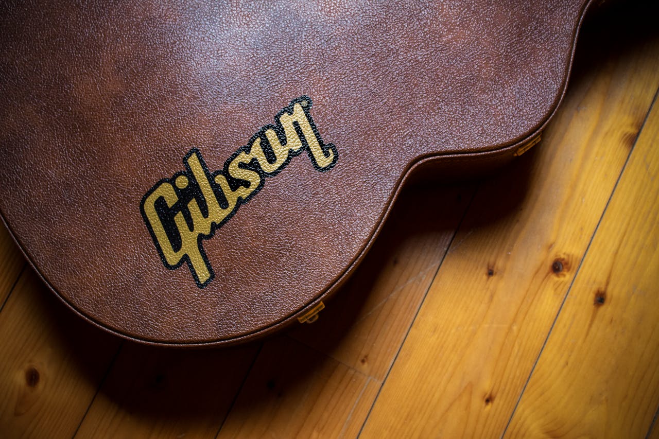 A close shot of a brown guitar case with 'Gibson' logo, placed on a wooden floor.